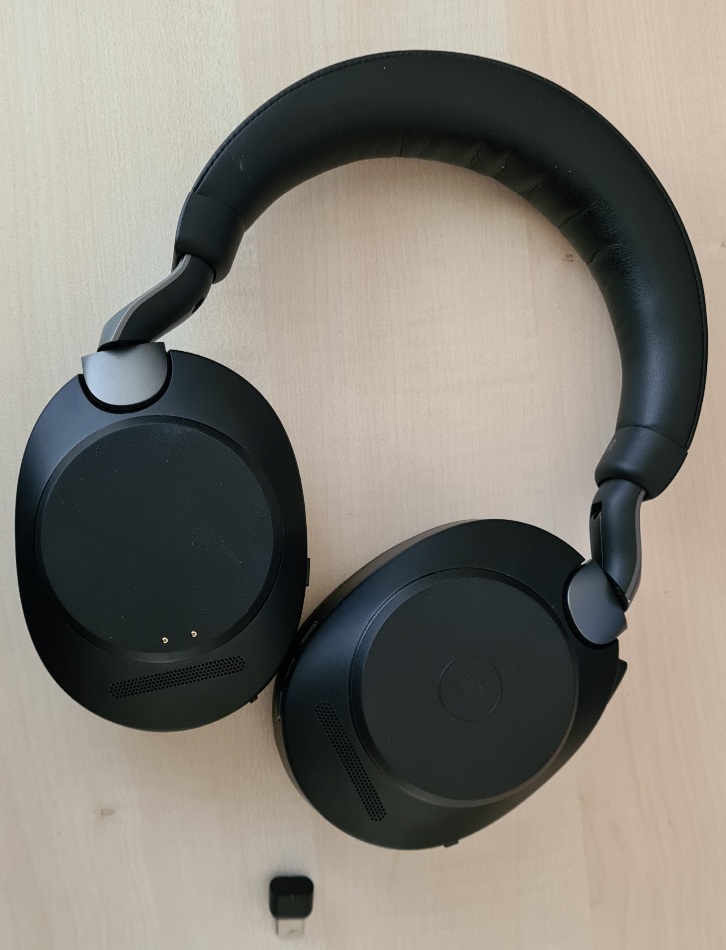 Photo of my Jabra Evolve 2 85 headphone and a USB-C dongle.  Both are black lying on a wooden table.